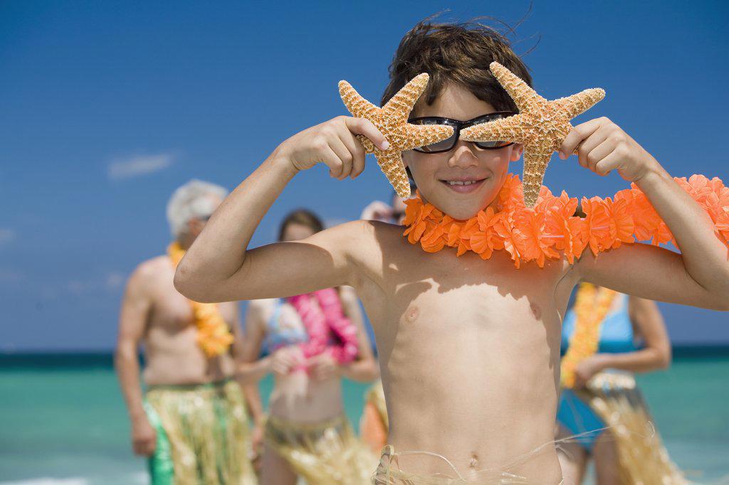 Close-up of a boy holding two starfish in front of his eyes with his grandparents and sister in the background