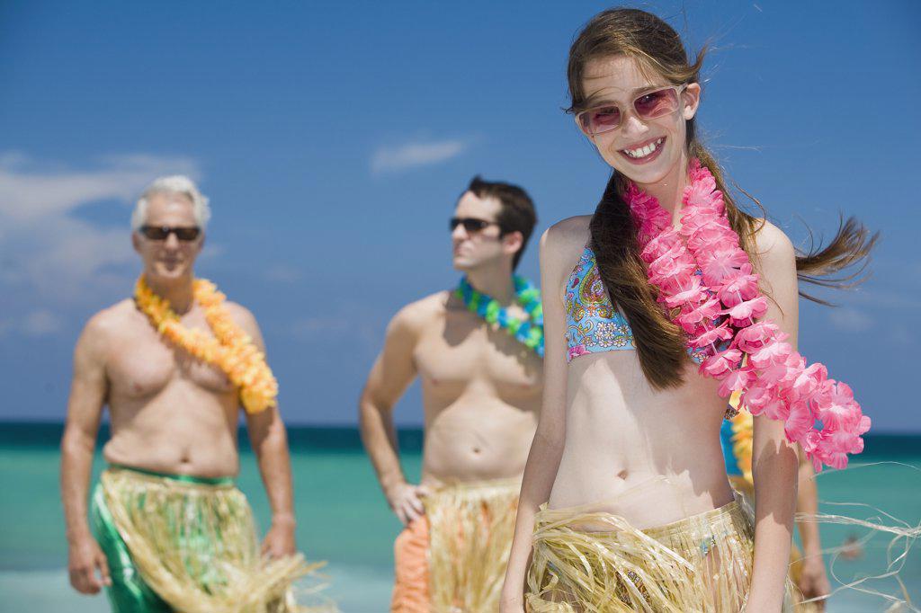 Close-up of a girl smiling with her grandfather and father standing behind her on the beach