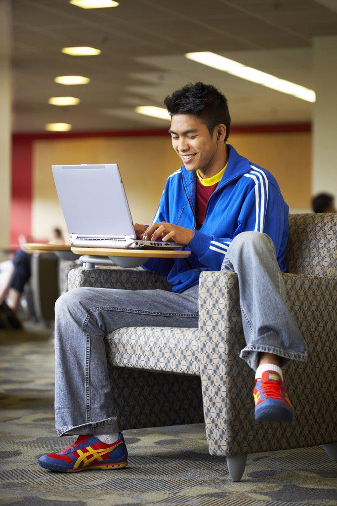 College student sitting in an armchair and using a laptop