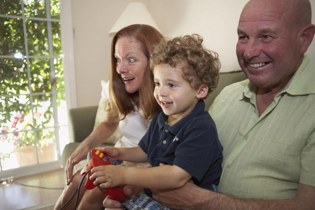 Close-up of a boy sitting with his grandparents and playing a video game