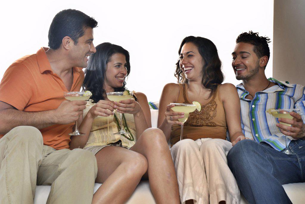 Mid adult couple and a young couple sitting on a couch and holding margaritas