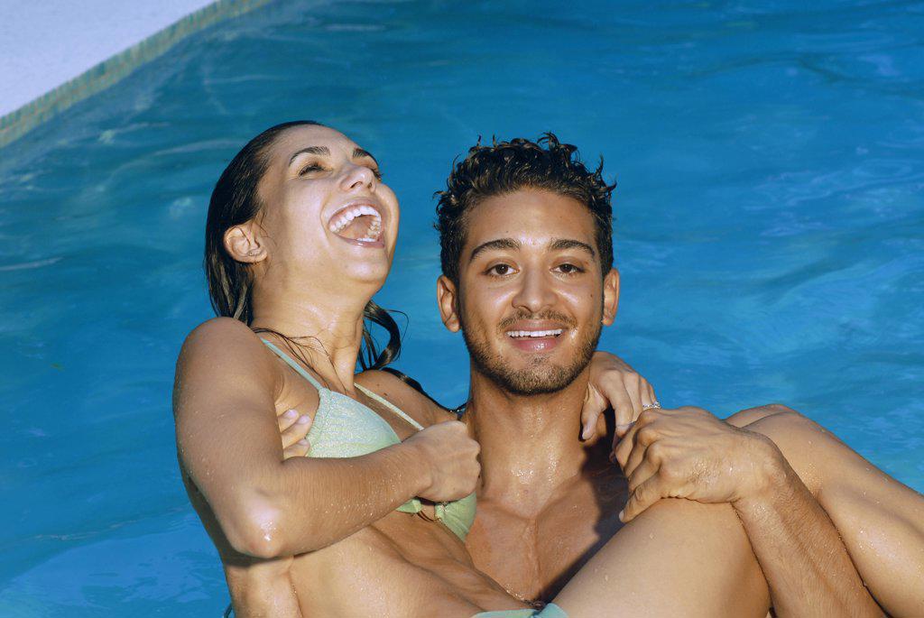 Portrait of a young man carrying a young woman in a swimming pool