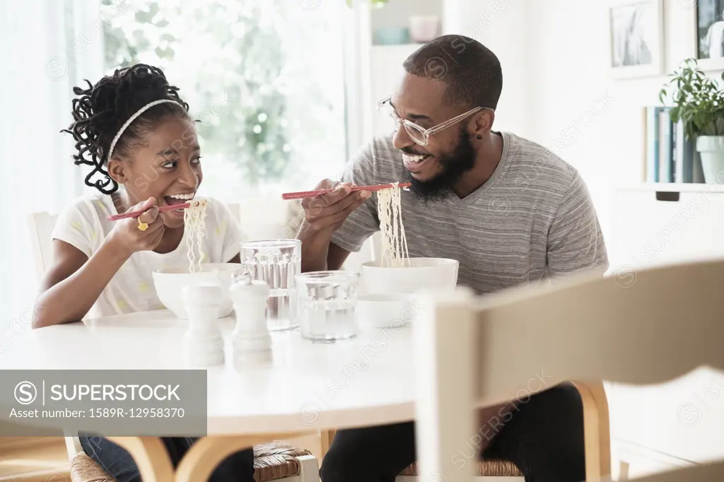 Black father and daughter eating noodles