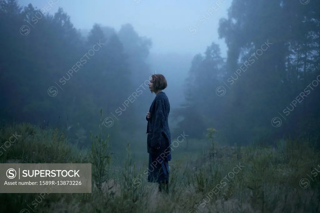 Pensive woman standing in fog in forest