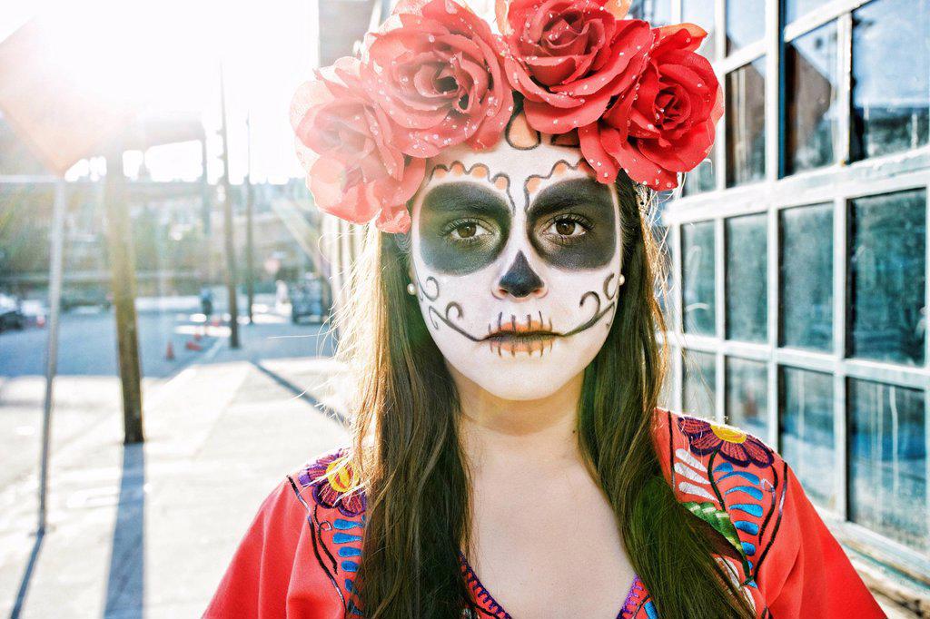 Hispanic woman on sidewalk wearing skull face paint