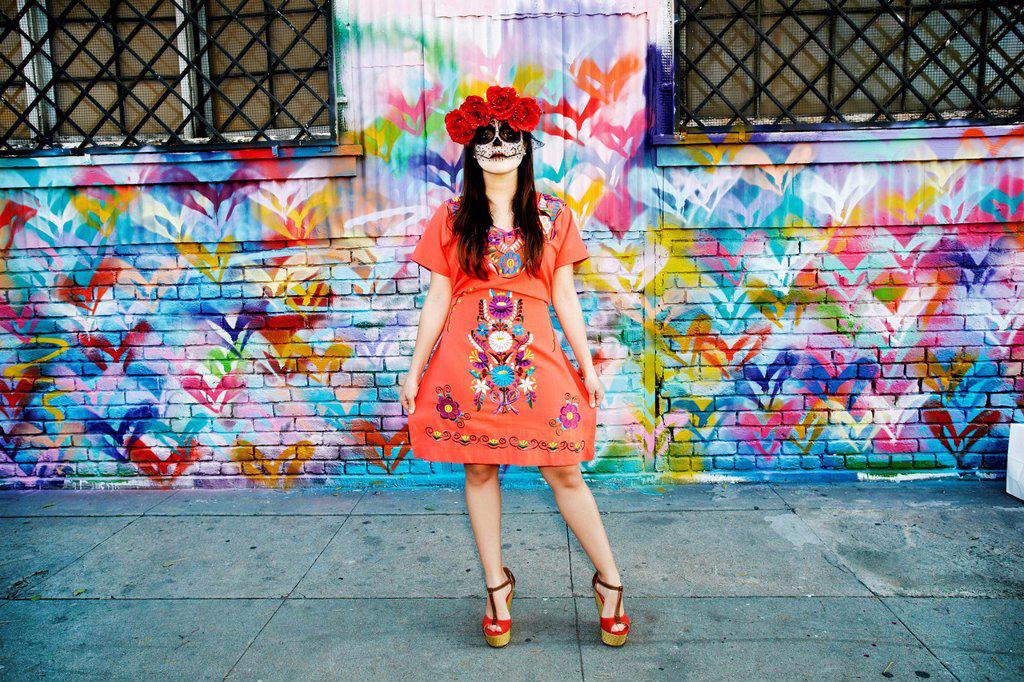 Hispanic woman standing on sidewalk wearing skull face paint