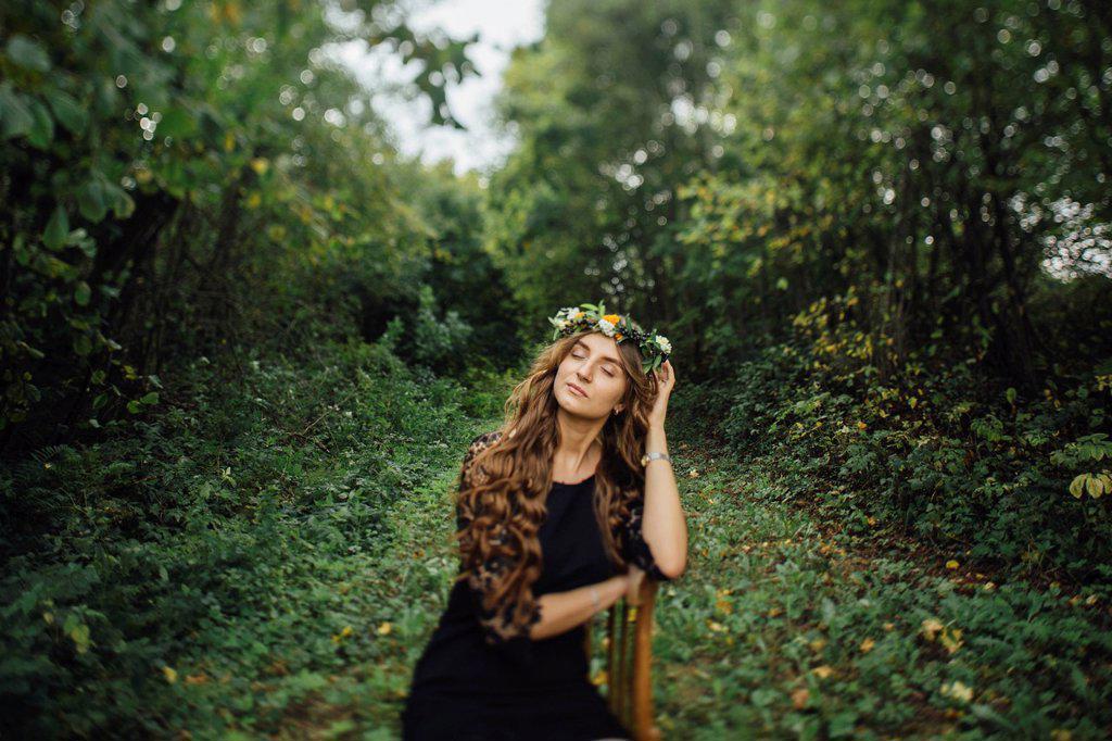 Middle Eastern woman wearing flower crown sitting on chair in woods