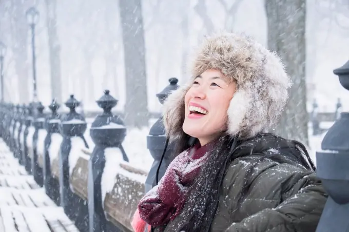 Asian woman sitting on park bench in snow