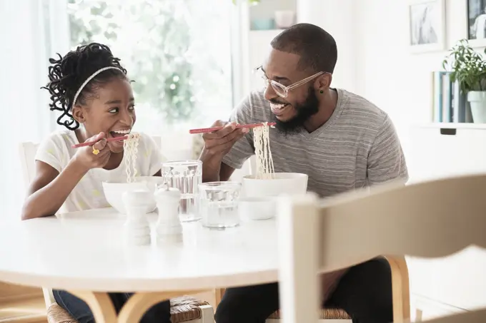 Black father and daughter eating noodles