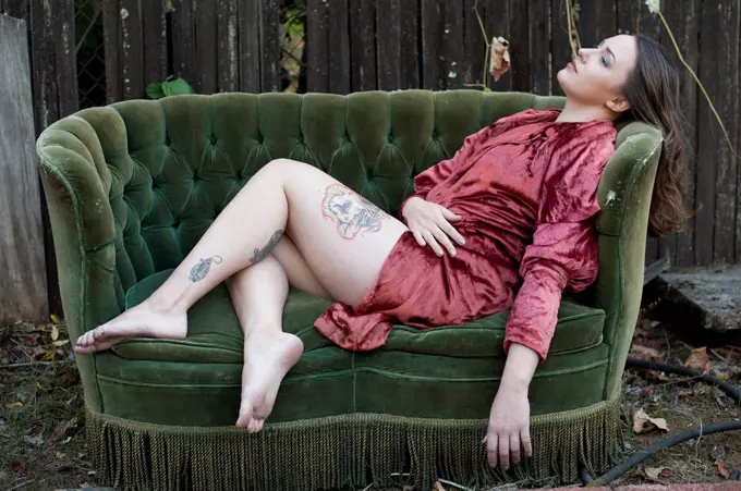 Caucasian woman with tattoos wearing bathrobe on backyard sofa