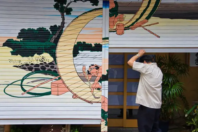 The owner opens the shutters of his traditional Japanese restaurant that are decorated with a Hokusai woodblock print in the Nihonbashi district of central Tokyo, Japan.