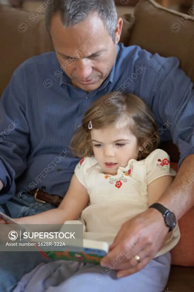 High angle view of a girl sitting with her grandfather and reading a book