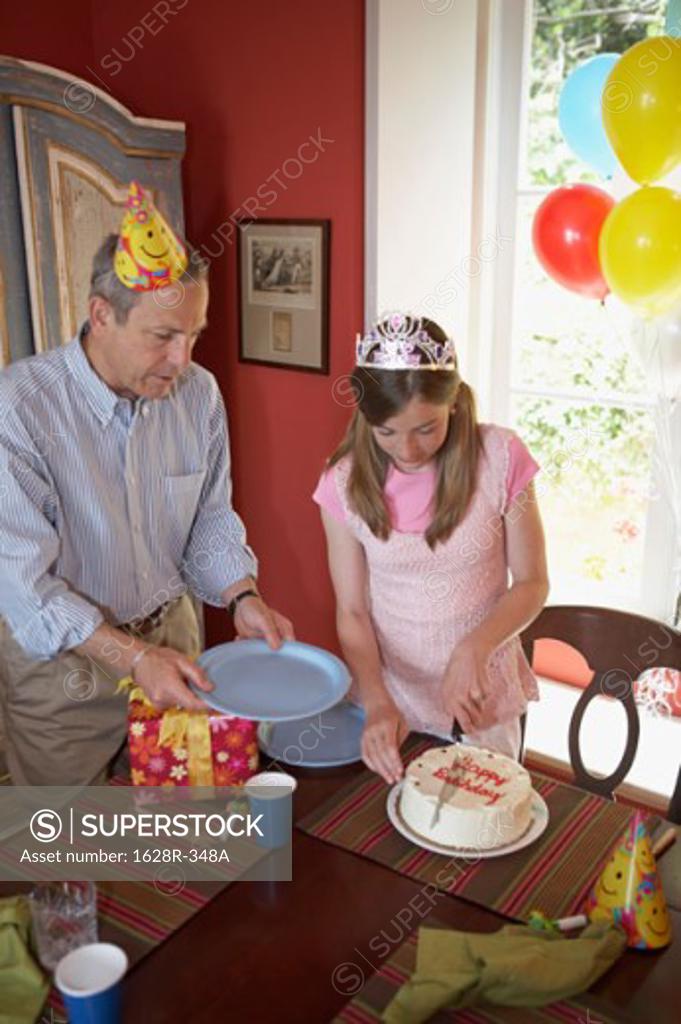 Stock Photo: 1628R-348A High angle view of a teenage girl cutting a birthday cake with her grandfather standing near her