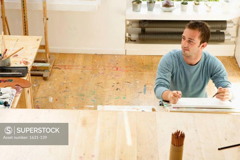 Stock Photo: 1631-139 Young man sitting at a table and holding a pencil