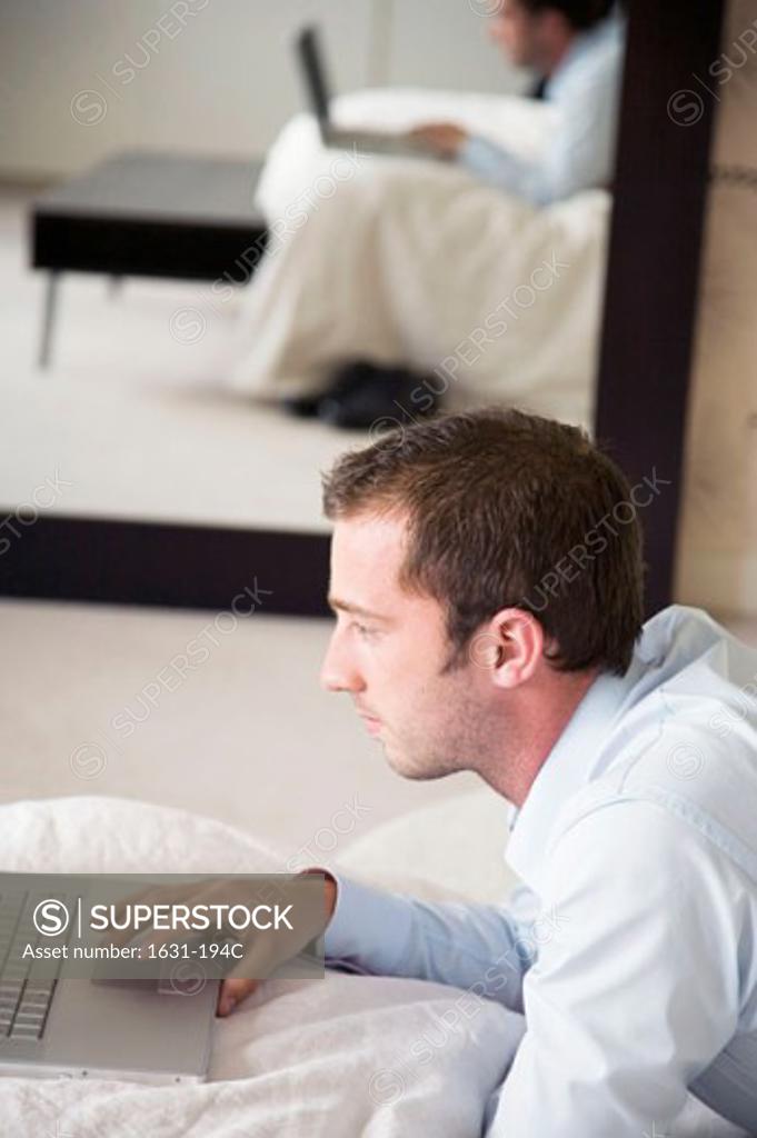 Stock Photo: 1631-194C Side profile of a young man lying on the bed and using a laptop