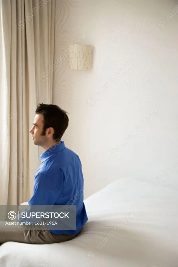 Side profile of a young man sitting on the bed