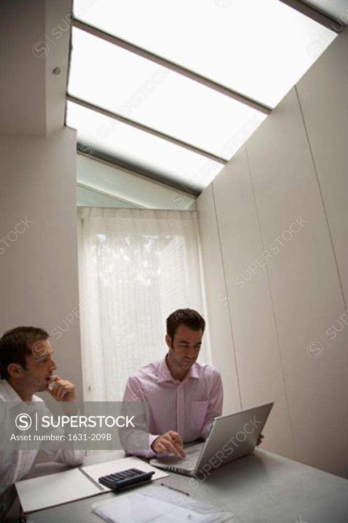 Stock Photo: 1631-209B Businessman using a laptop with another businessman sitting beside him