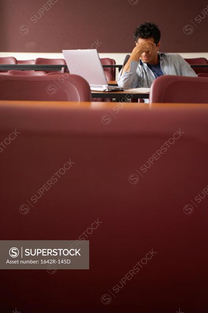 Stock Photo: 1642R-145D College student sitting in a lecture hall with his hand on his forehead