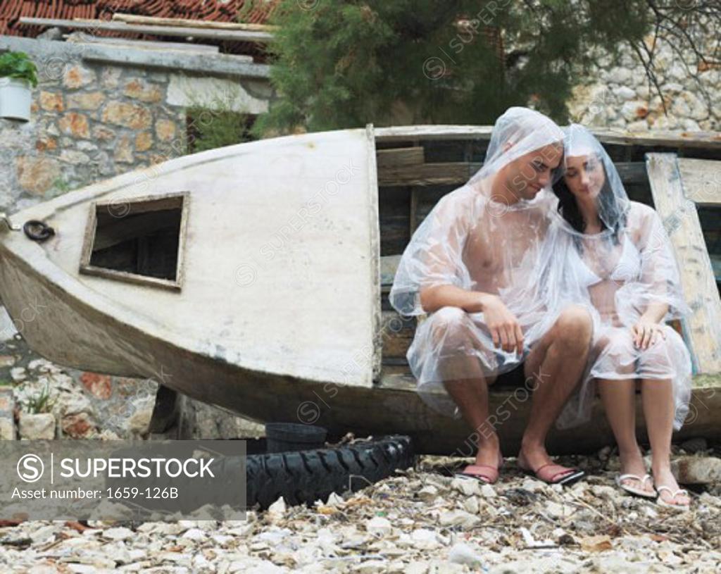 Stock Photo: 1659-126B Young couple wearing raincoats and sitting on a boat