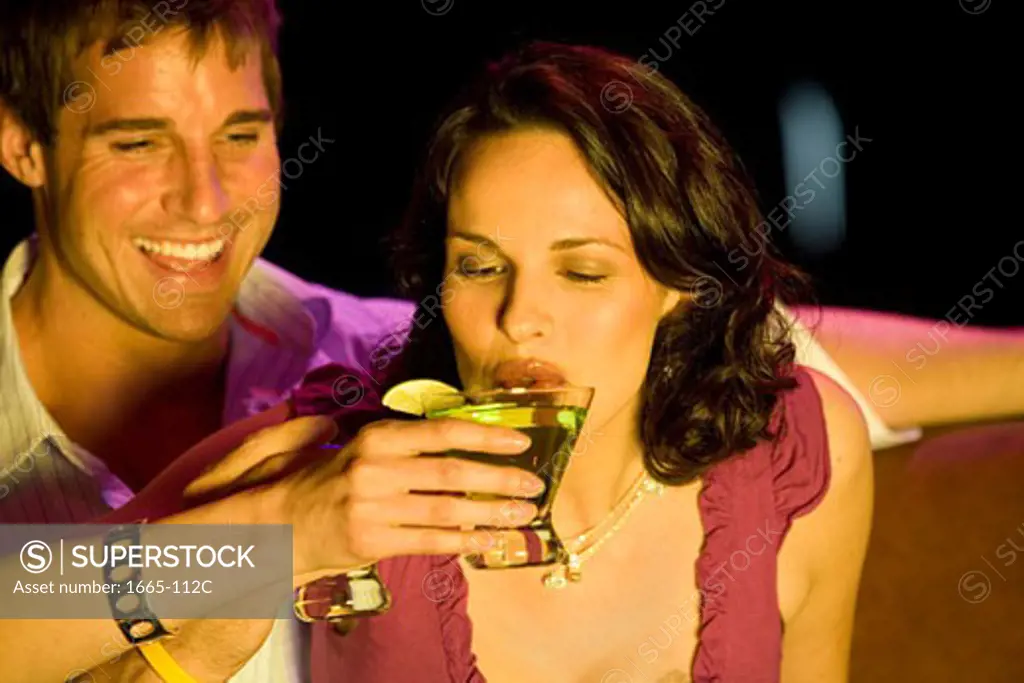 Close-up of a young woman drinking a cocktail and a young man looking at her