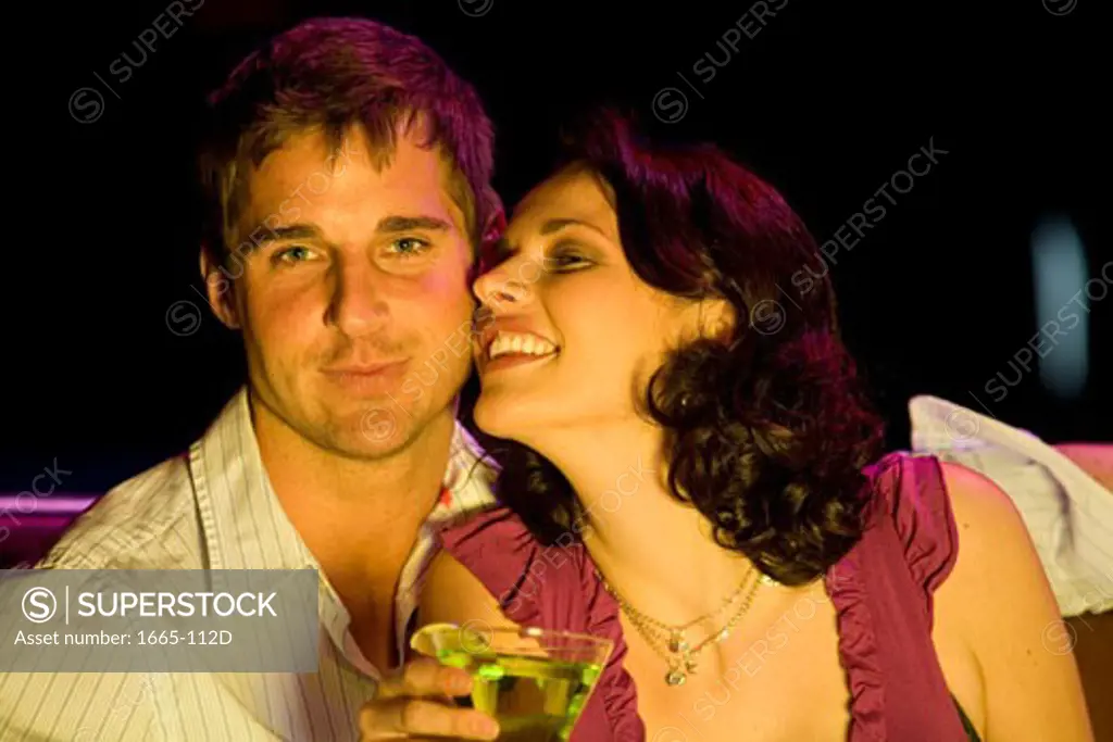 Close-up of a young woman sitting with a young man and holding a cocktail