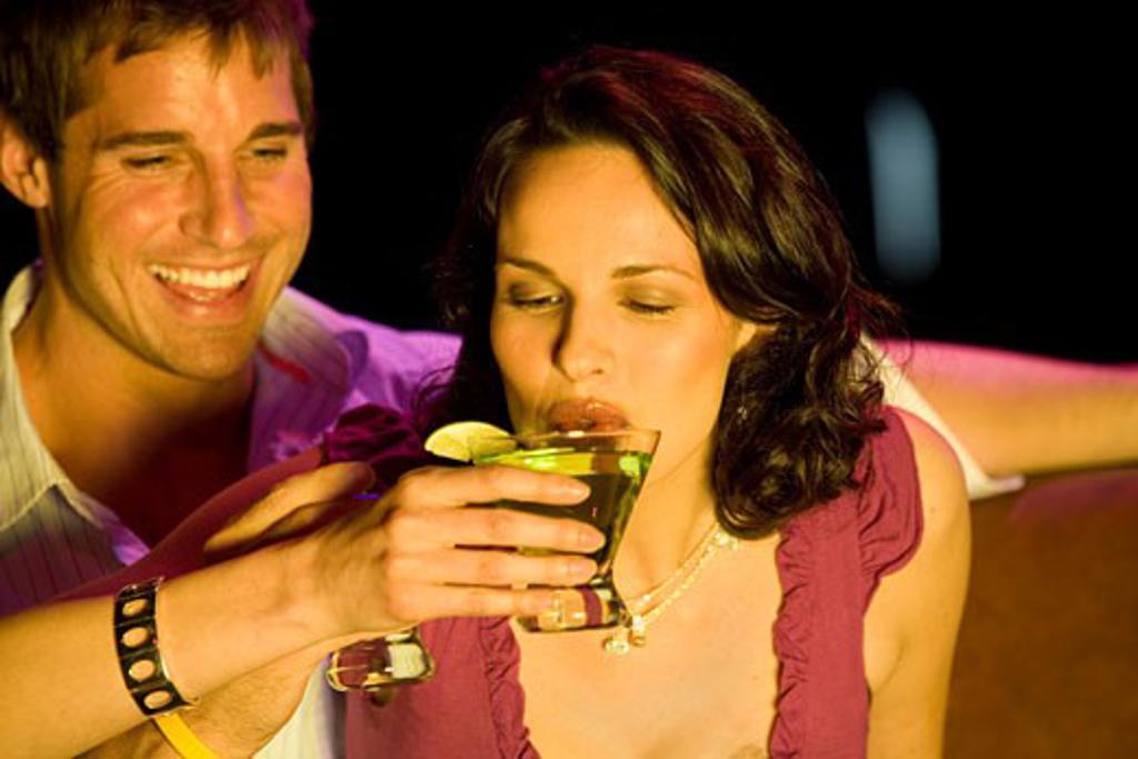 Close-up of a young woman drinking a cocktail and a young man looking at her