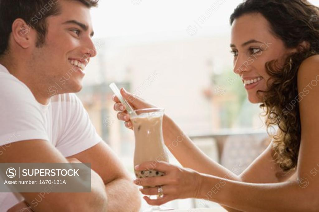 Stock Photo: 1670-121A Side profile of a young woman holding a milkshake with a teenage boy sitting in front of her