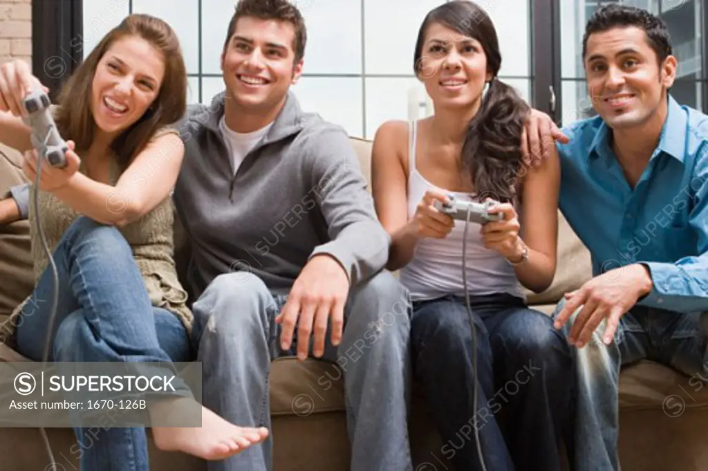 Two young women playing video game with a teenage boy and a young man sitting beside them