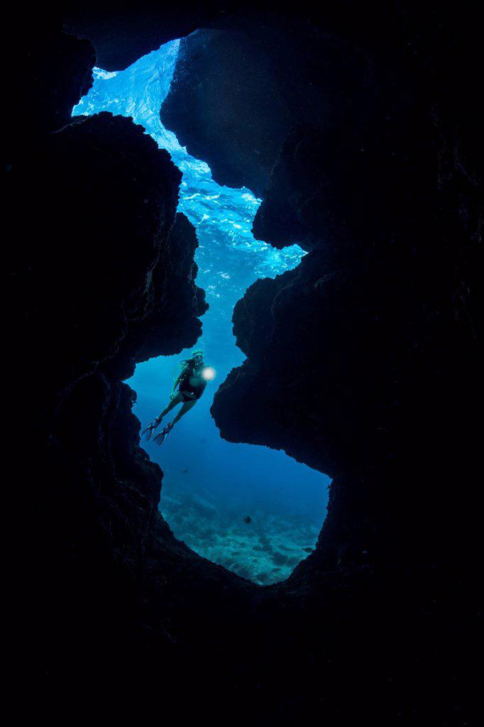 A diver (MR) shines her light into a crevice opening off Kaiwe Point on the Kona coast; Island of Hawaii, Hawaii, United States of America