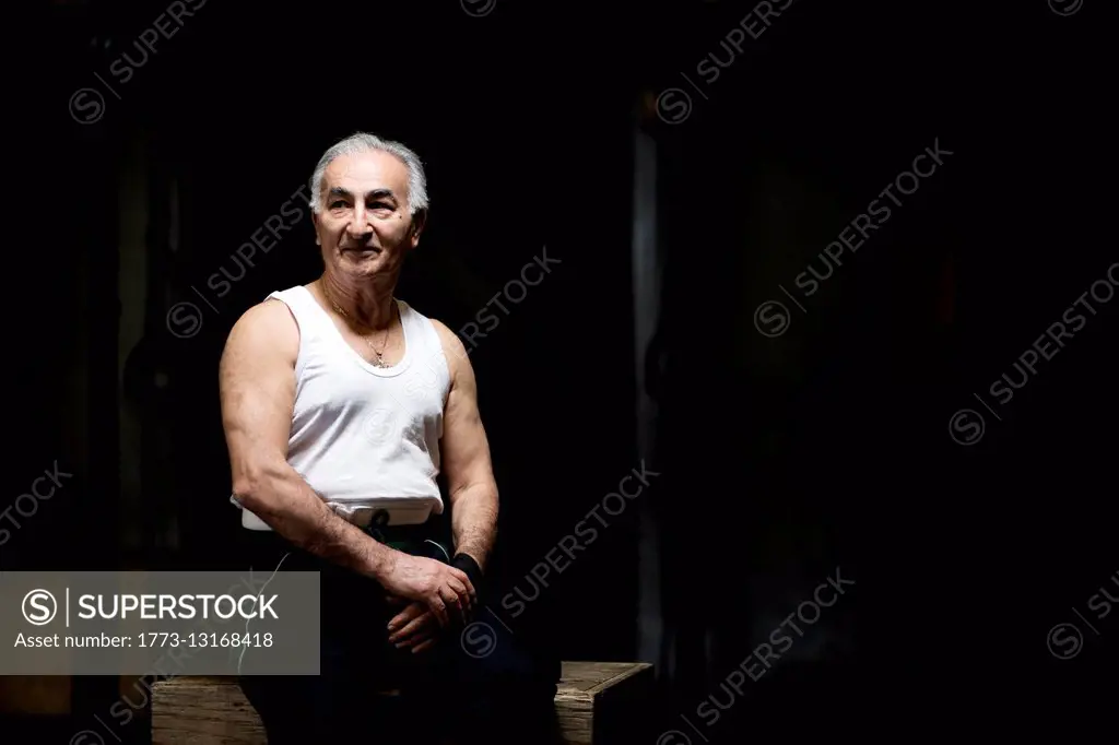 Portrait of grey haired senior man sitting in dark gym