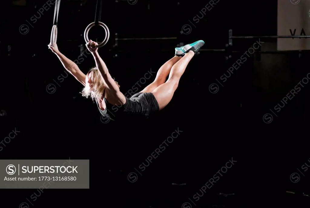 Young woman swinging on gym rings in dark gym