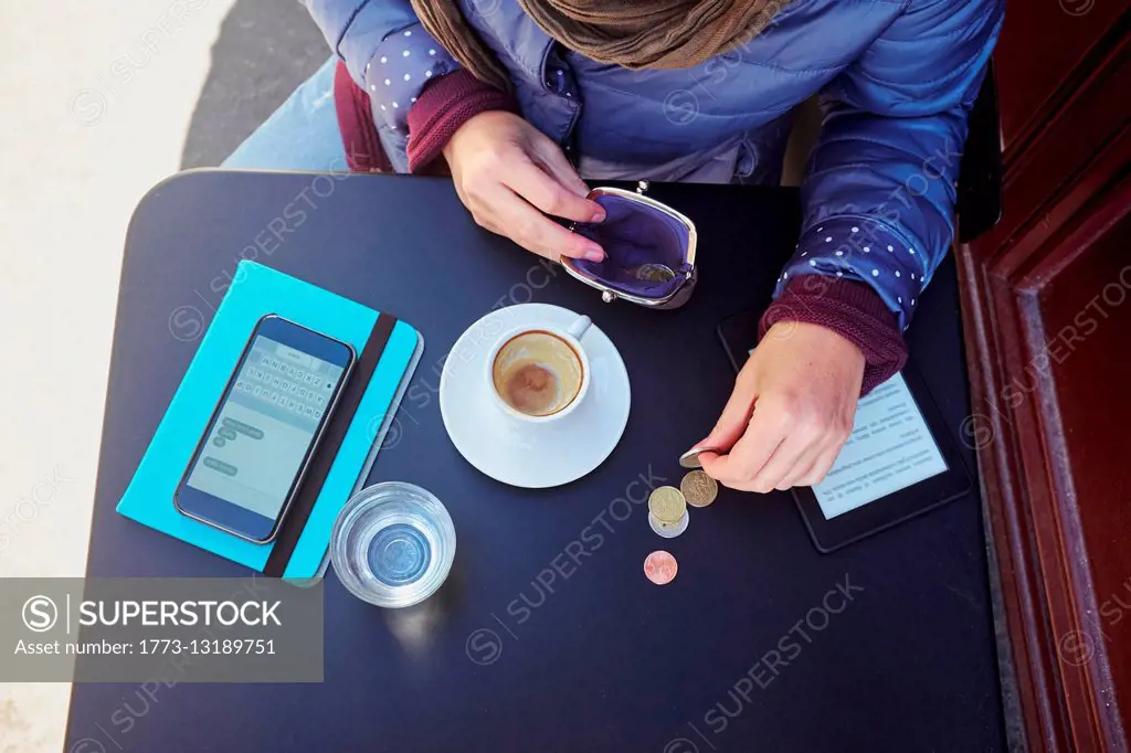 High angle view of mid adult woman counting euro coins at sidewalk cafe