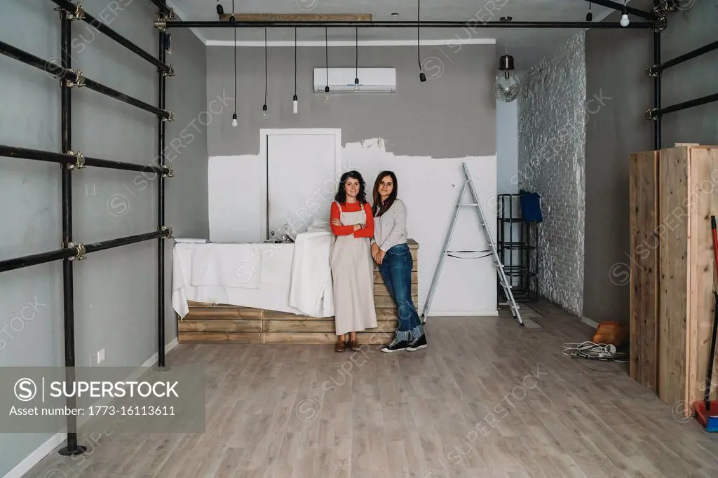 Two mid adult women leaning against table in their new shop, full length portrait
