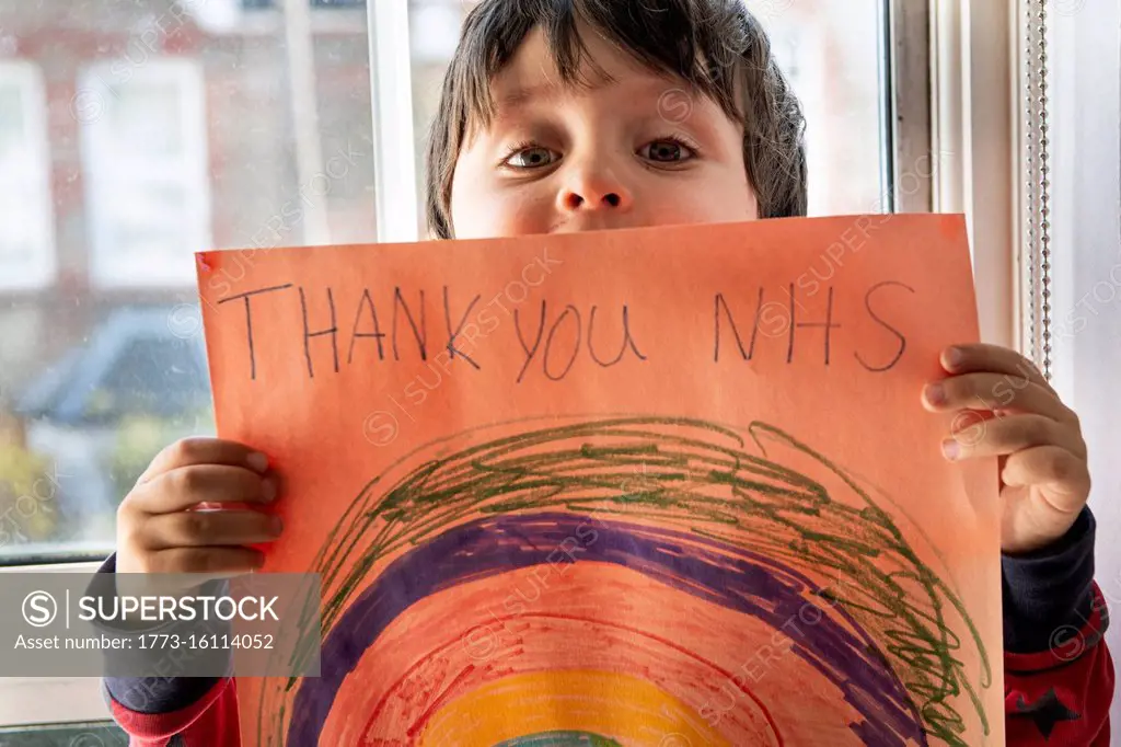 A boy holding up a drawing of a rainbow with the words Thank You NHS