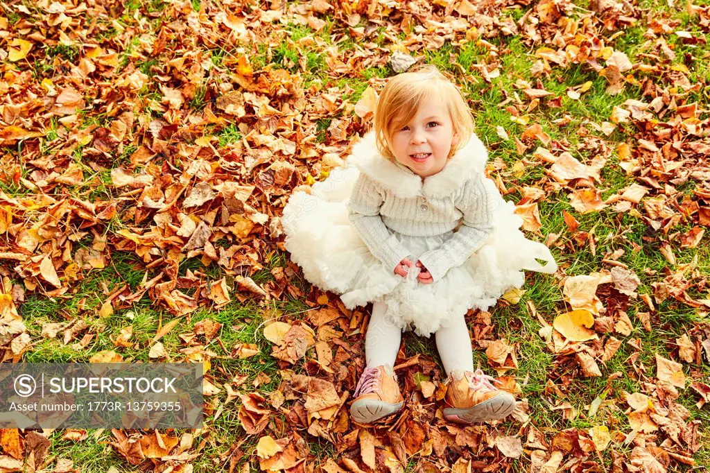Portrait of girl sitting in autumn leaves looking at camera smiling