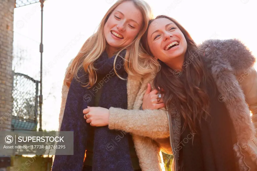 Two female friends outdoors, walking arm in arm, laughing
