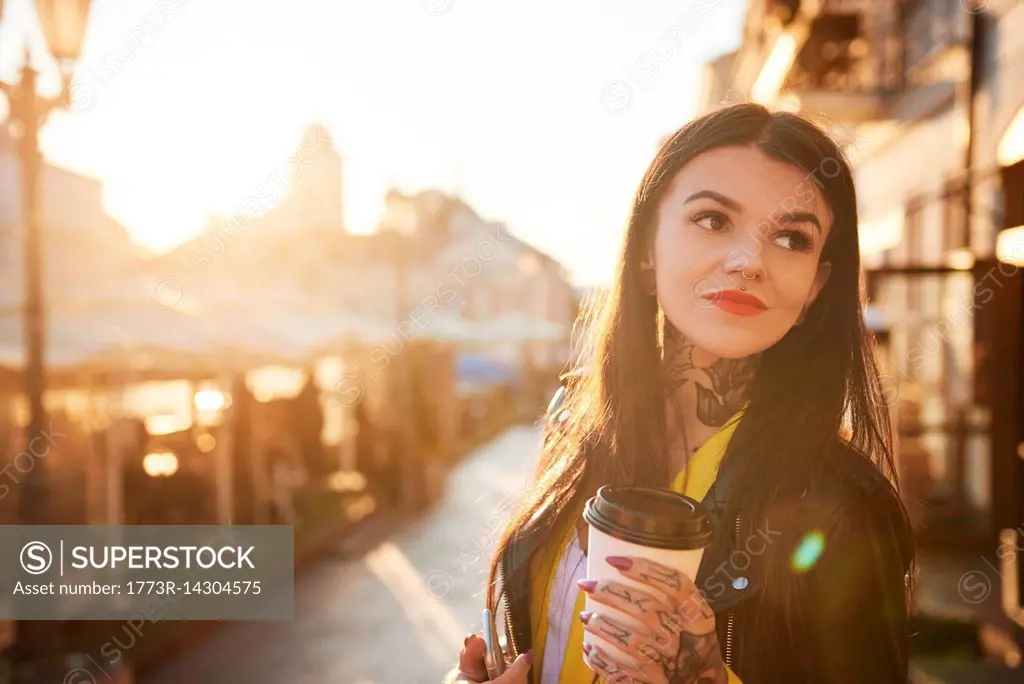 Young woman outdoors, holding coffee cup, tattoos on hands and neck