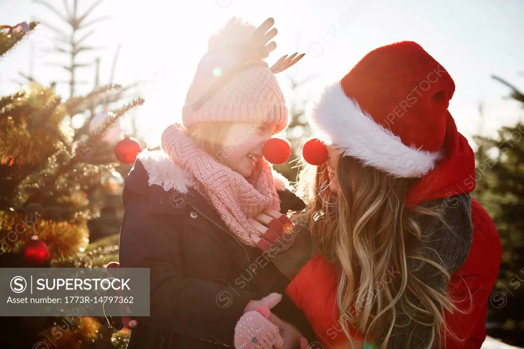 Girl and mother in christmas tree forest wearing red noses