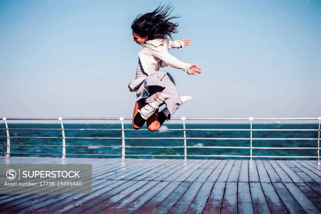 Mid adult woman jumping mid air on sea pier, Odessa, Odeska Oblast, Ukraine