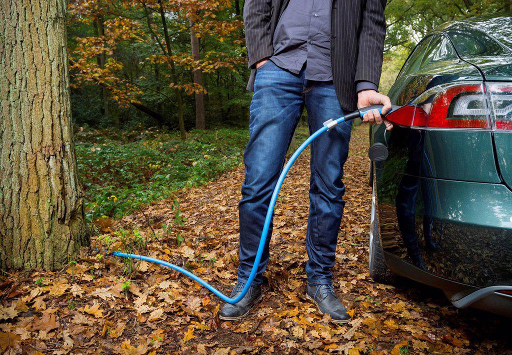 Man charging electric car in forest