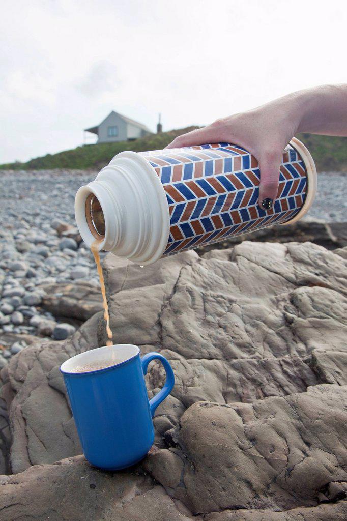 Female hand pouring tea from drinks flask on Millook Beach, Cornwall, UK
