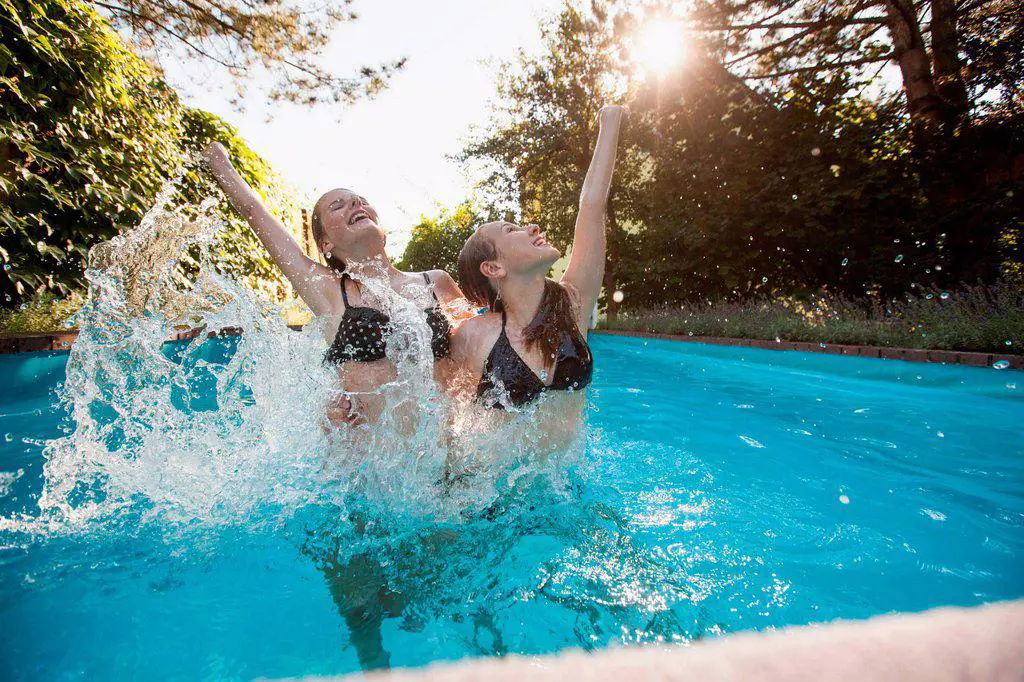 Two teenage girls jumping with arms raised in swimming pool