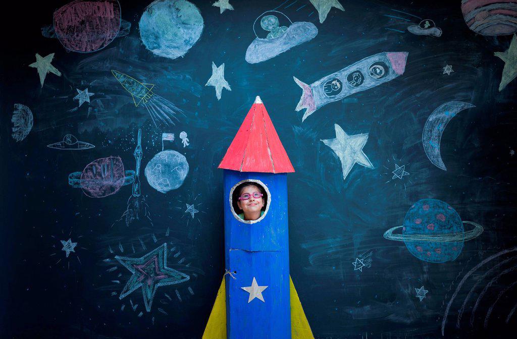 Portrait of girl in handmade space rocket in front of space themed chalk drawings
