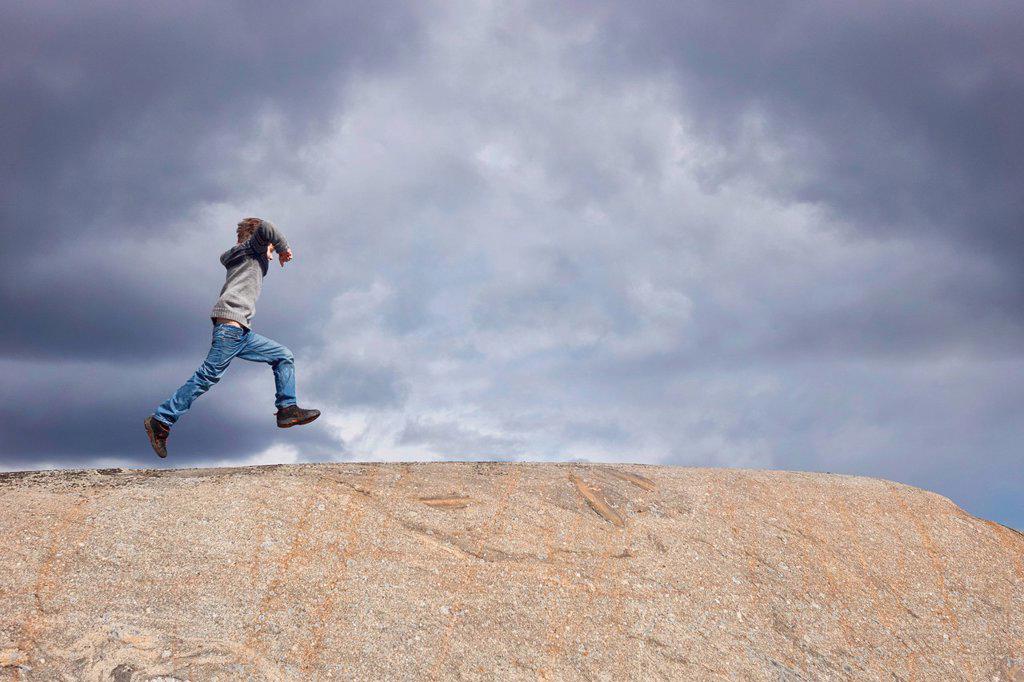Boy running on top of rock against stormy cloud sky