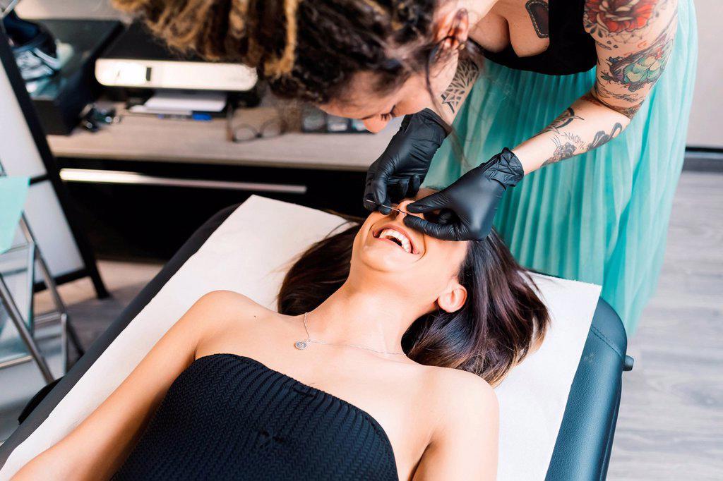 Tattooist piercing nose of customer in parlour