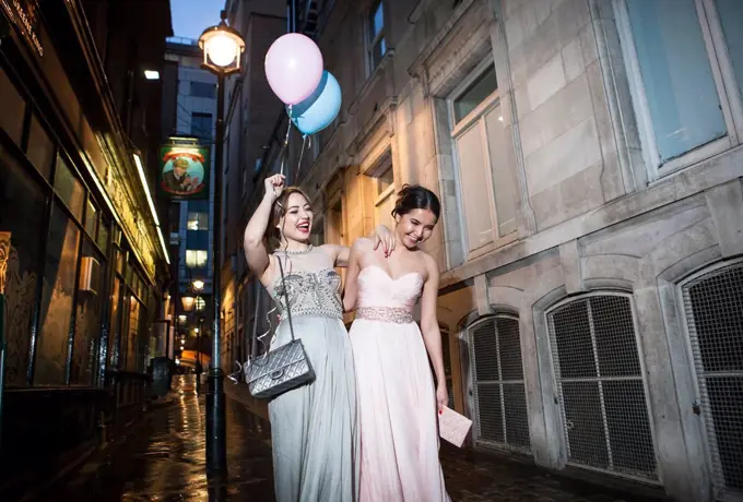 Two female friends in evening gowns having fun night out in city