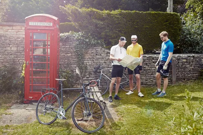 Cyclists map reading by red telephone box, Cotswolds, UK