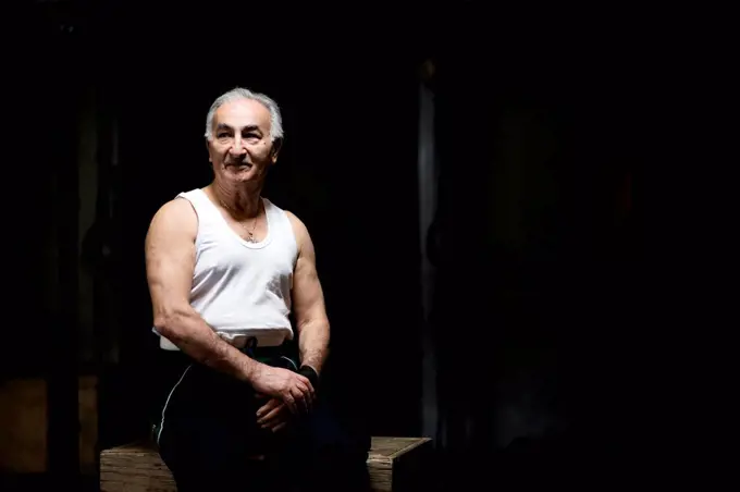 Portrait of grey haired senior man sitting in dark gym
