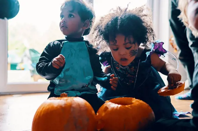 Two young children dressed up for Halloween kneeling on the floor with two pumpkins.