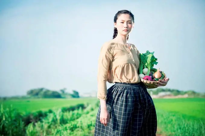 Young woman in field holding basket of homegrown vegetables